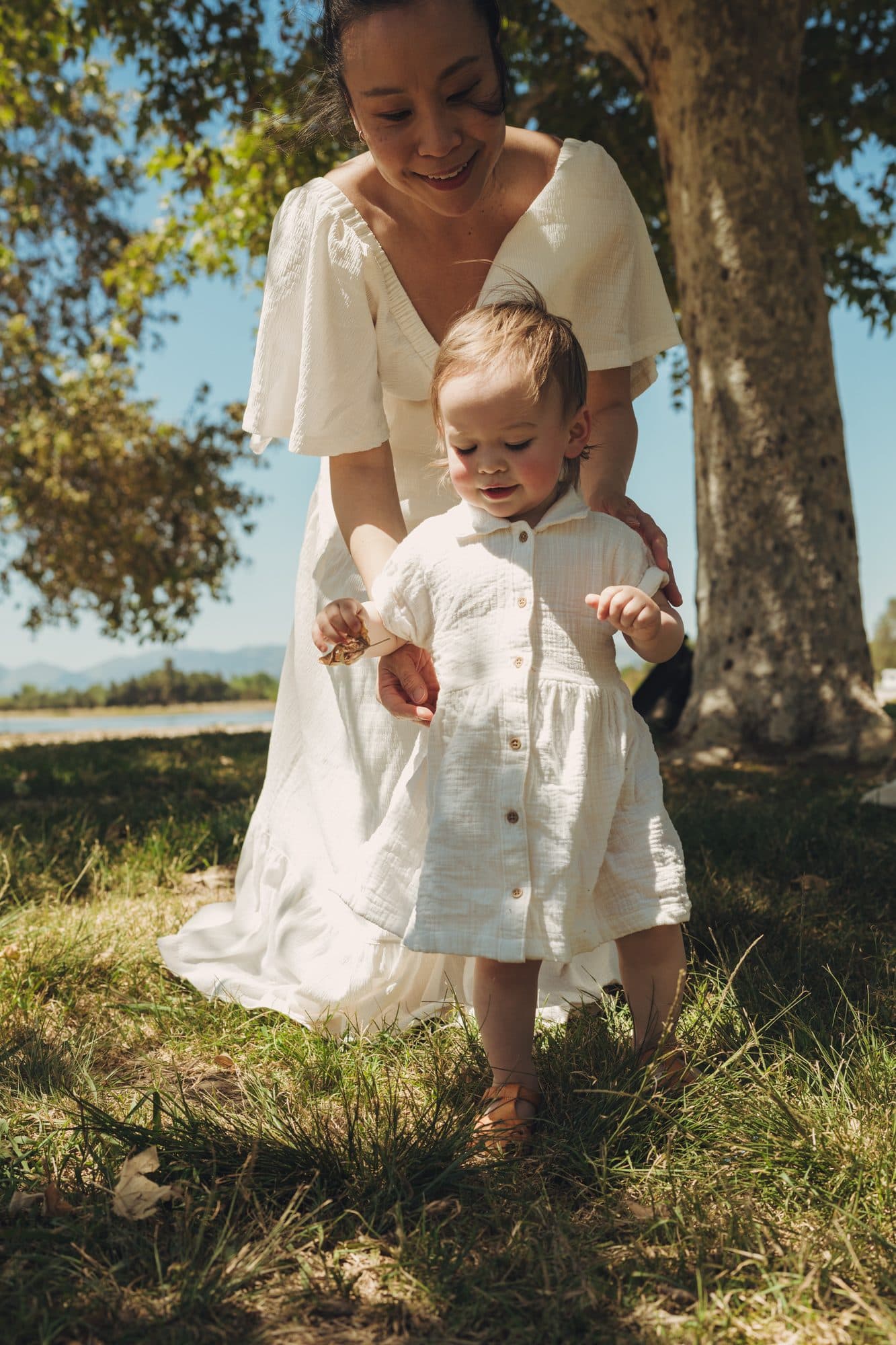 Mother in a white dress walking with her child under a tree