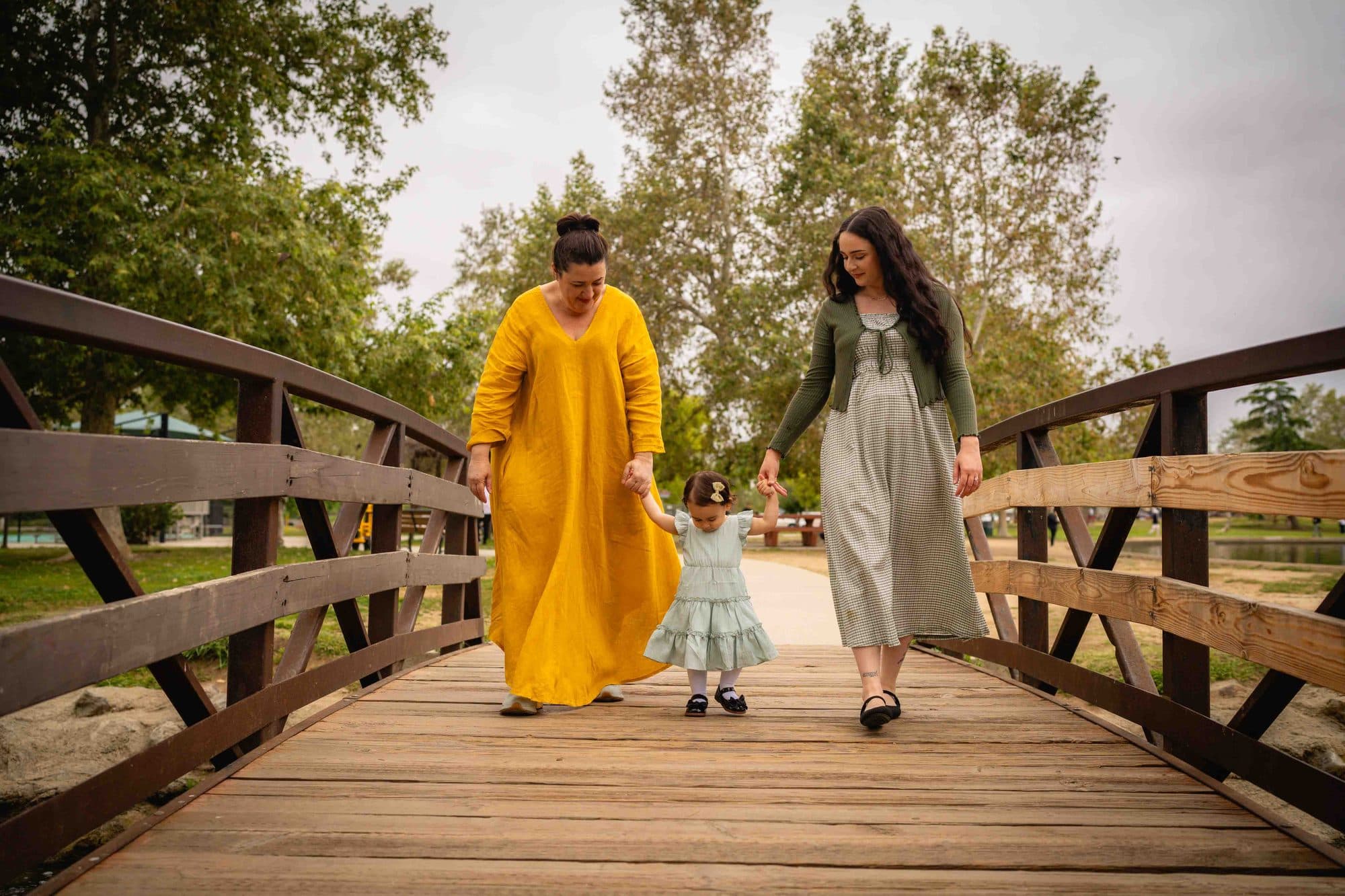 Mother in a yellow dress and her daughters on a park bridge